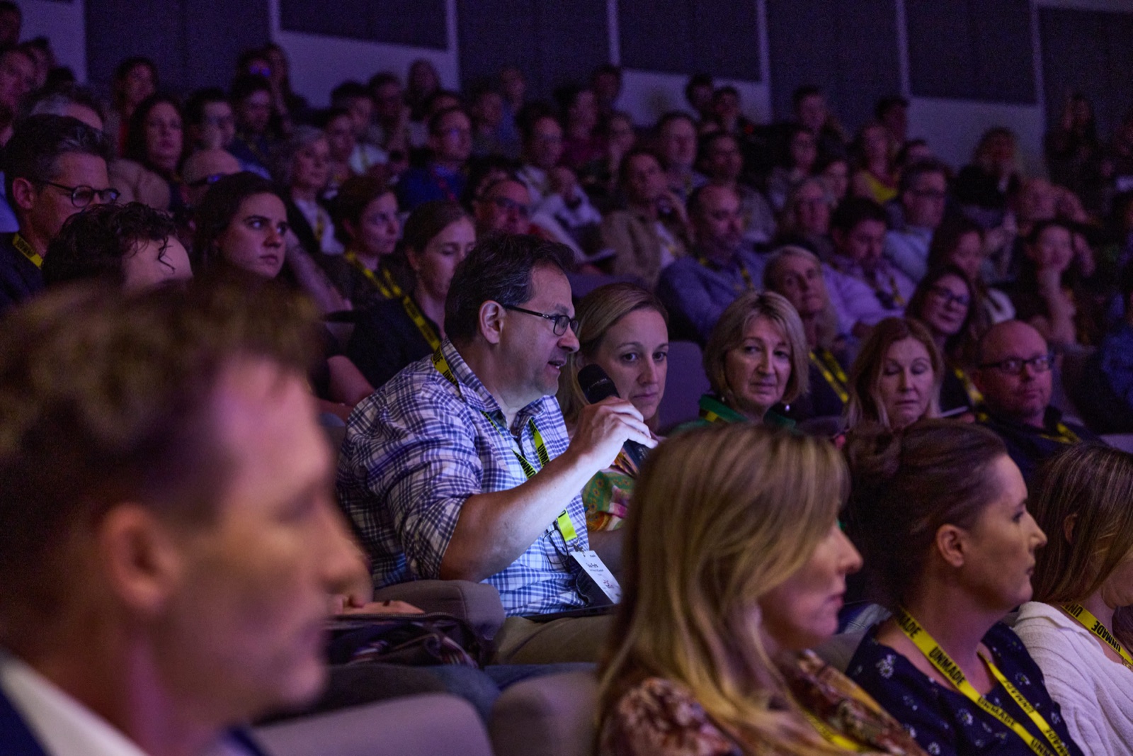 Audience member speaking into a microphone during Q&A in a packed auditorium
