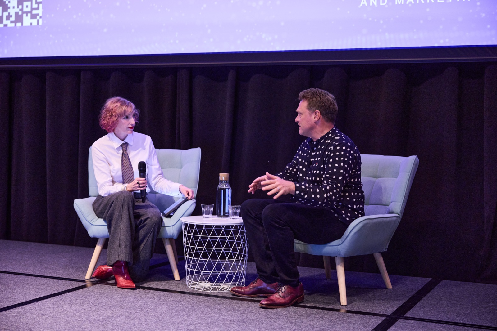 Host in conversation with a guest speaker in armchairs on stage