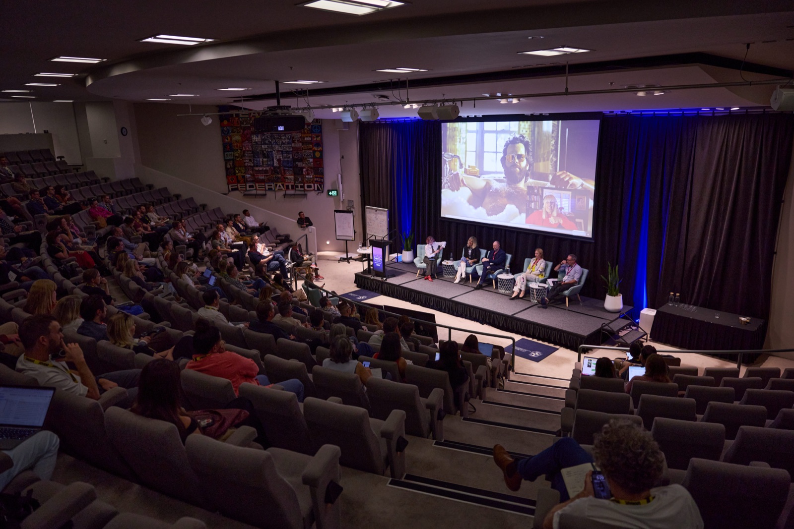 Aerial view of a full auditorium watching a panel session with AI film content on screen