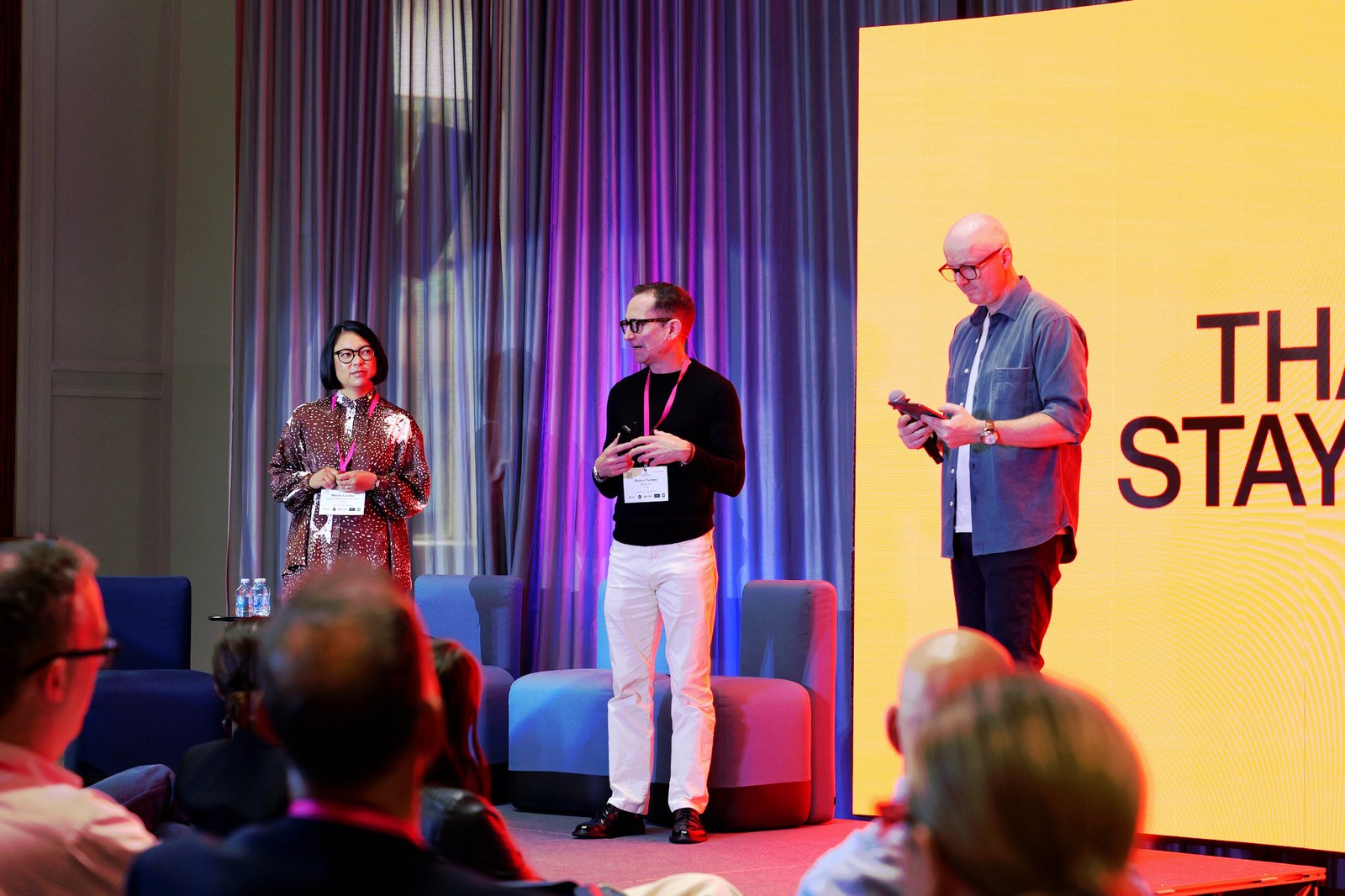 Three speakers on stage in front of a bright yellow screen