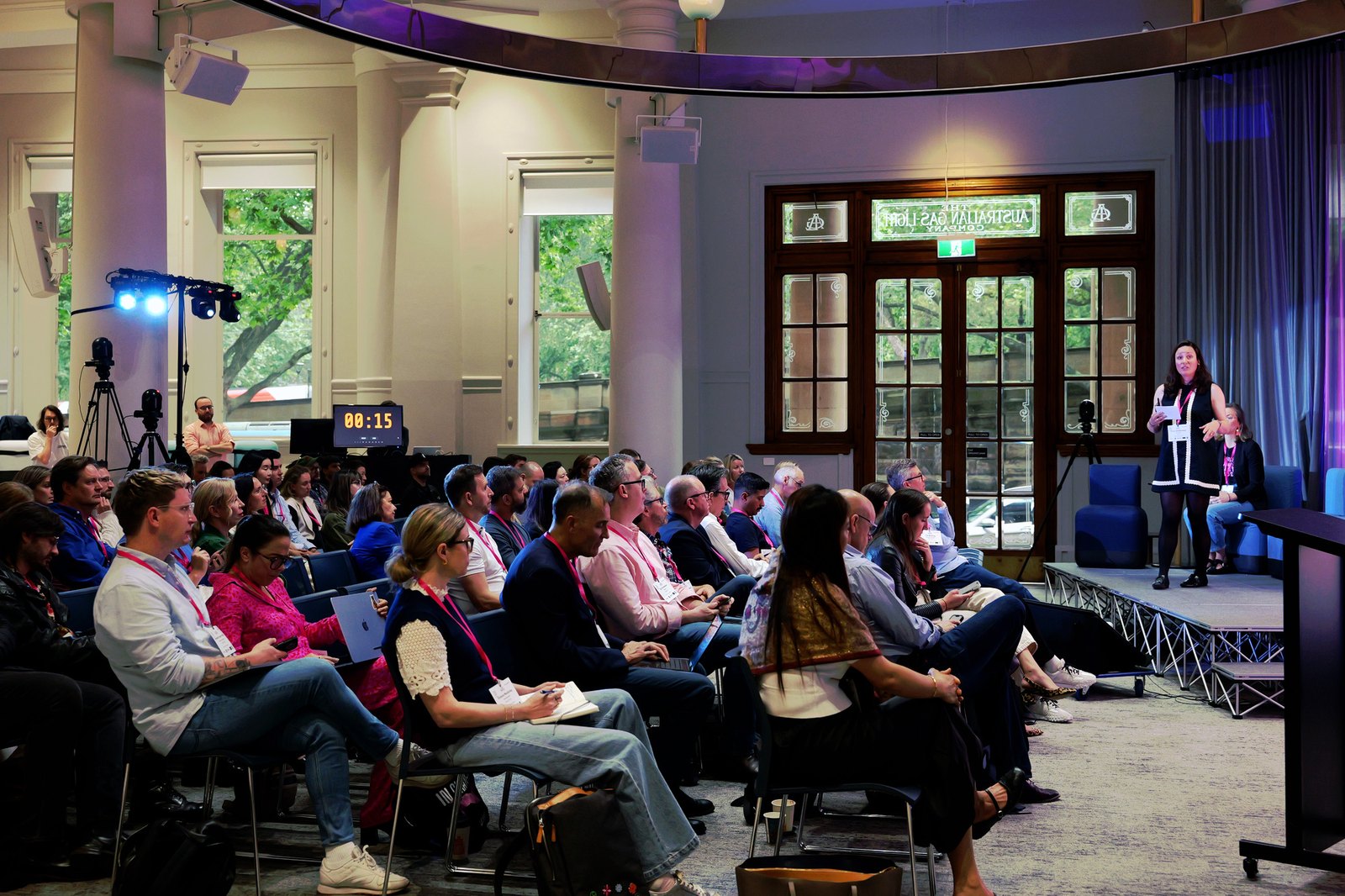 Wide view of the room with a woman on stage, the audience seated and a countdown clock at the back
