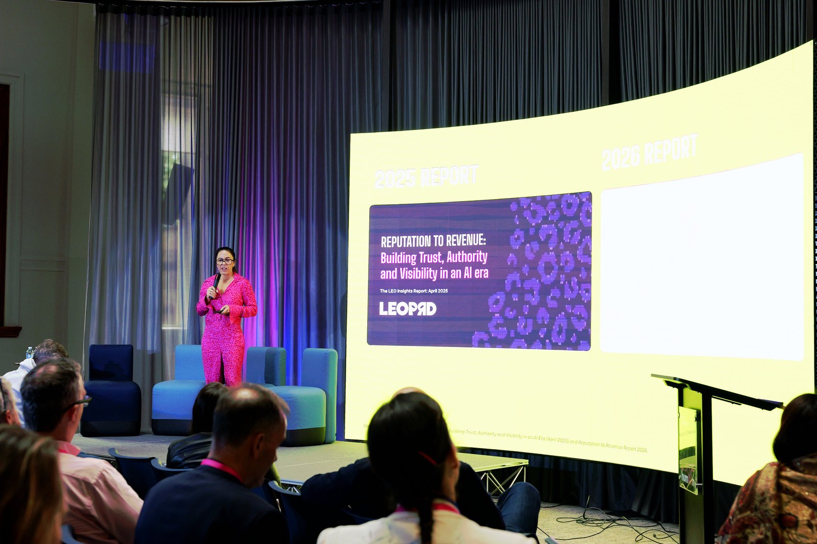 A woman in a pink suit presenting in front of a slide titled "Reputation to Revenue"