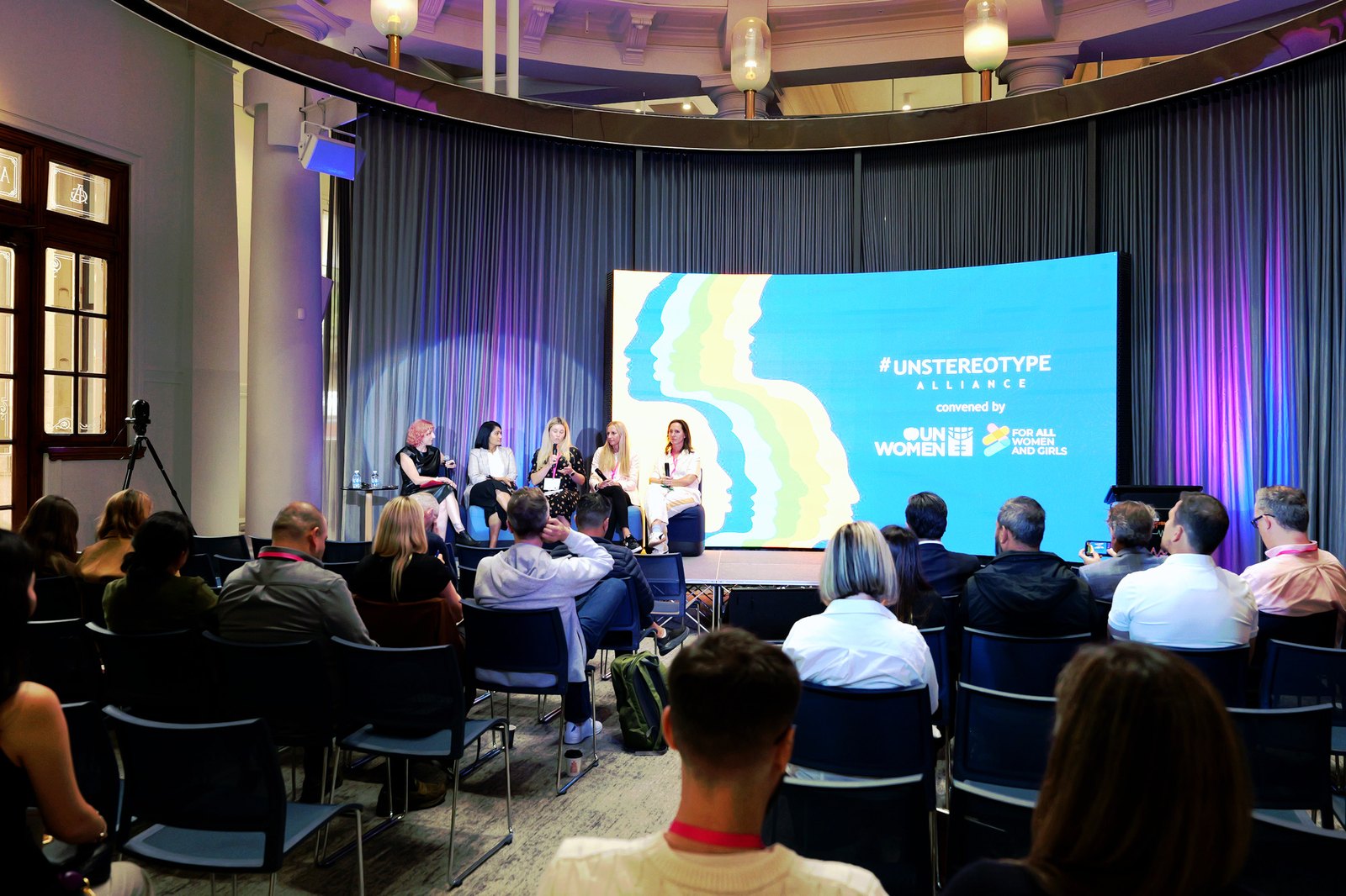 Wide view of a panel on stage in front of an Unstereotype Alliance slide, with the audience seated in front