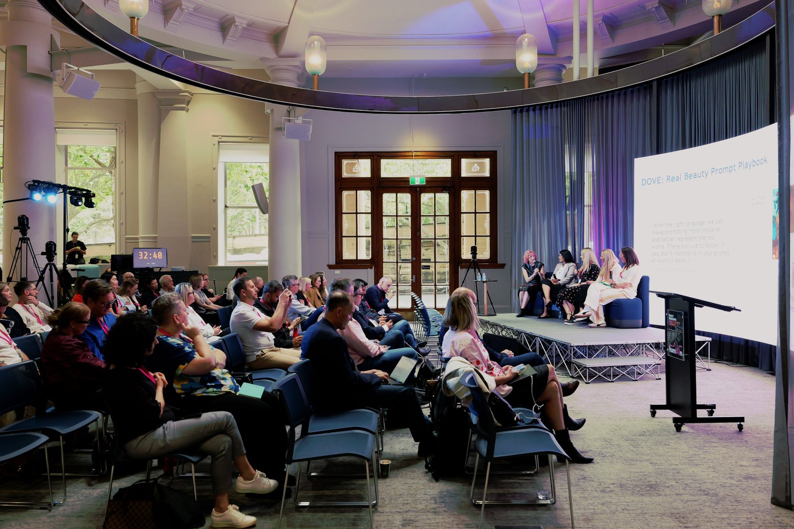 Wide view of the room with a panel on stage and the audience seated