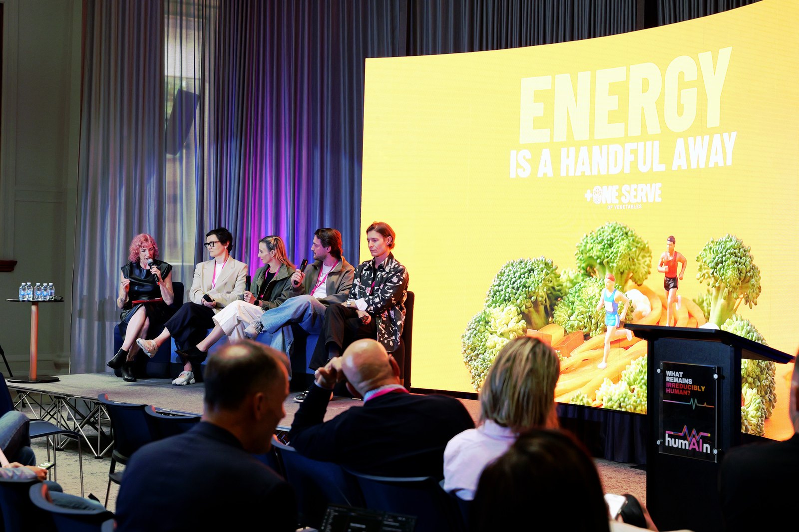 Cat McGinn and a panel seated on stage in front of a yellow "Energy is a handful away" slide