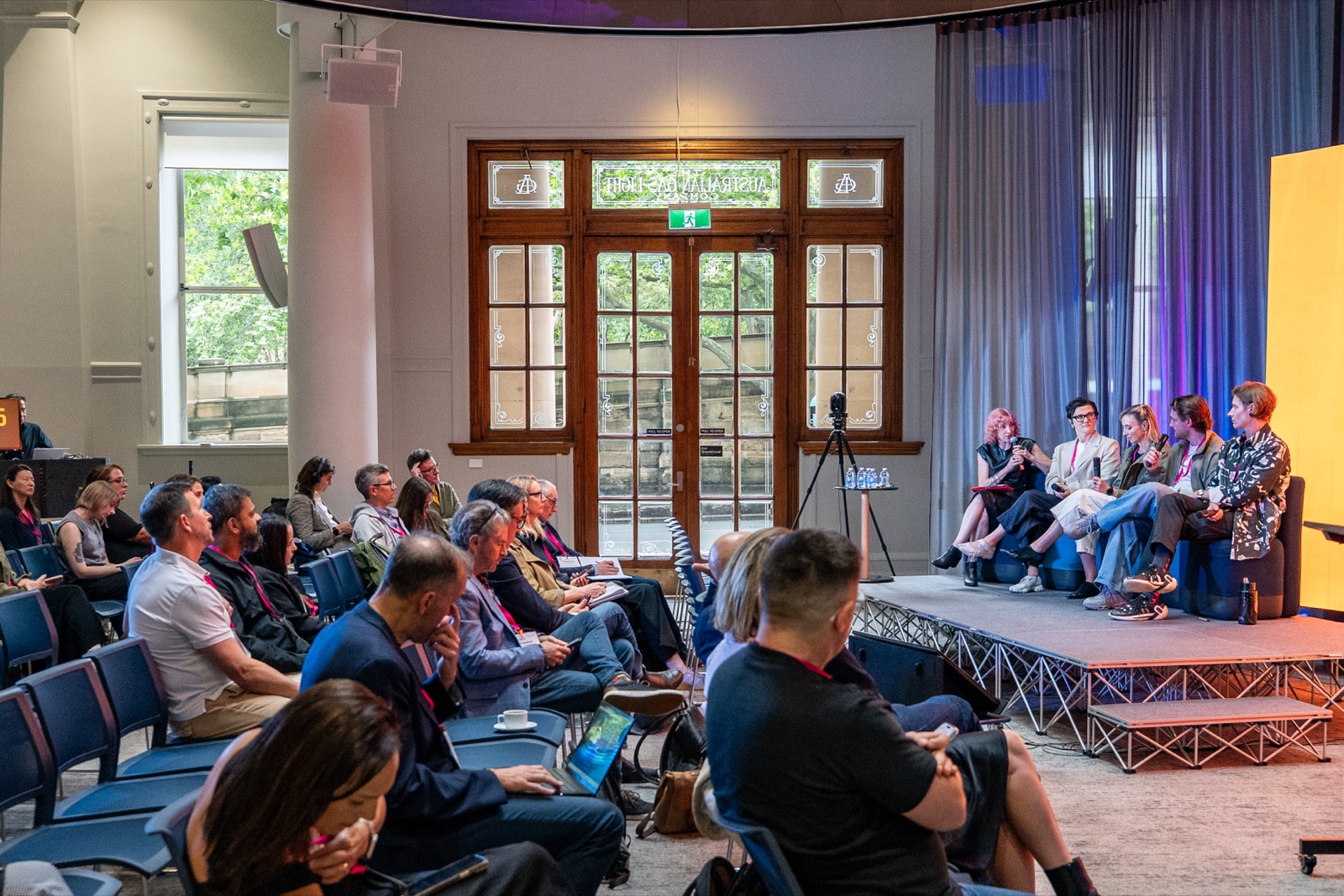 Wide view of the room with the audience seated facing a panel on stage