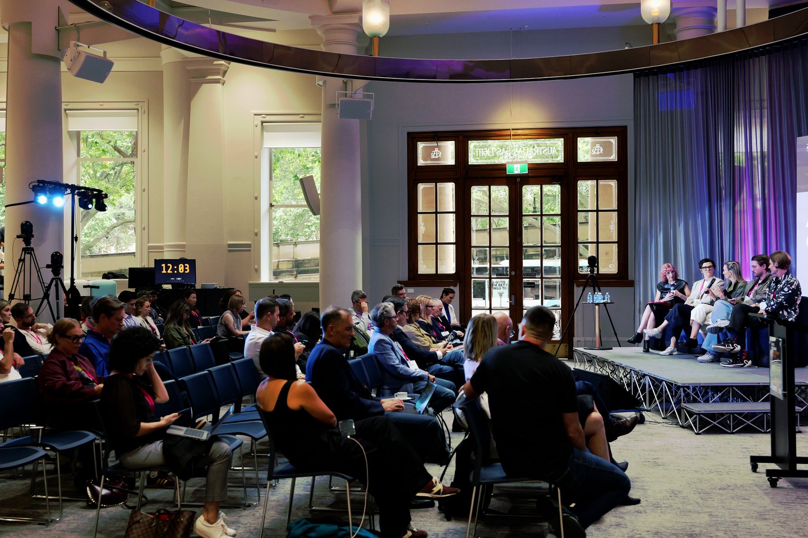 Wide view of the room with a panel on stage and the audience seated