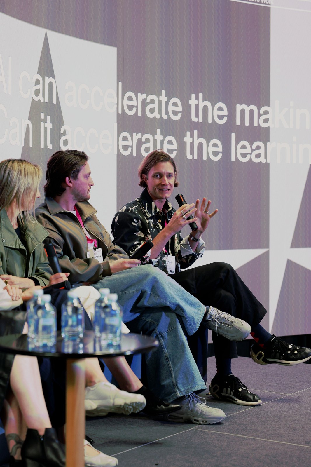 Panellists in conversation in front of a slide reading "AI can accelerate the making"